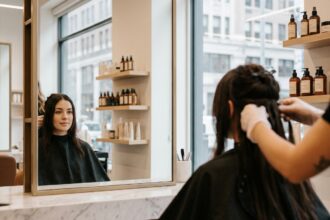 Femme en salon de coiffure lors de la pose d'extensions de cheveux naturels, vue de trois quarts dans un miroir