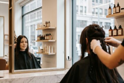 Femme en salon de coiffure lors de la pose d'extensions de cheveux naturels, vue de trois quarts dans un miroir